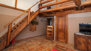 A wooden staircase with a red carpet, a wooden cabinet with a TV, and a shelf with glassware.
