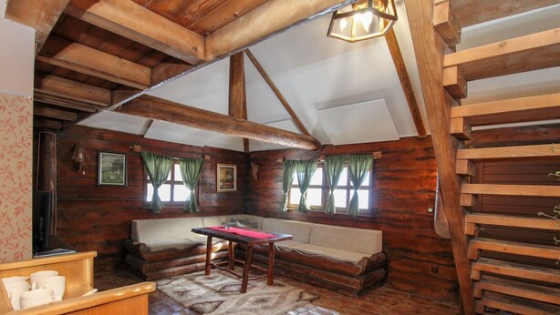 A rustic cabin interior with a wooden bench, a table, and a fireplace.