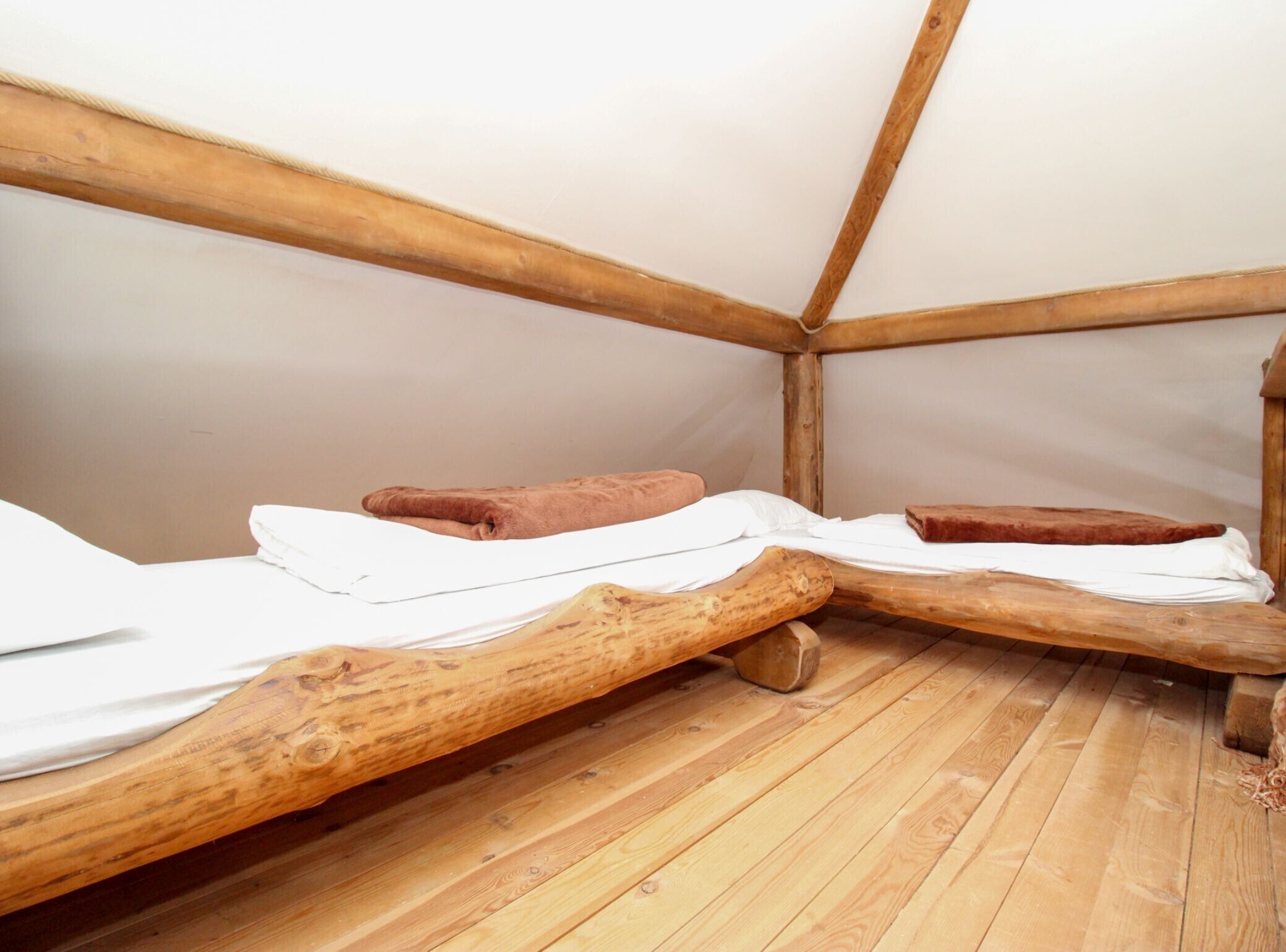 A small, wooden tent-style room with two beds and a wooden floor.