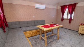 Une pièce avec un canapé gris, une table en bois surmontée d’un chemin de table rouge et une fenêtre ornée de rideaux rouges.