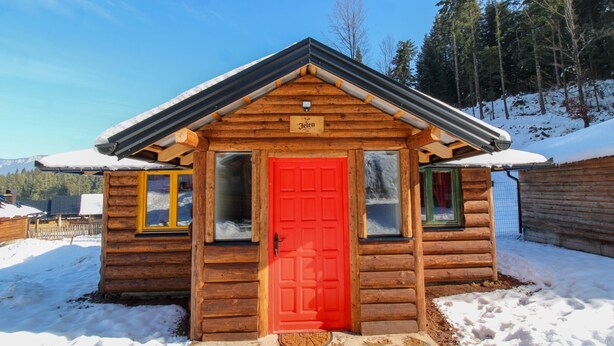 Une petite cabane en bois avec une porte rouge, une fenêtre et une enseigne au-dessus de la porte.