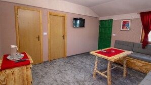 Une pièce avec une table en bois, un canapé gris, une porte verte et un téléviseur fixé au mur.