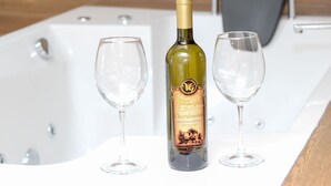 A bottle of wine and two glasses on a white surface in front of a bathtub. - Ethno Village Dolina Mira - One Bedroom Holiday Home (Drina) (Pale)