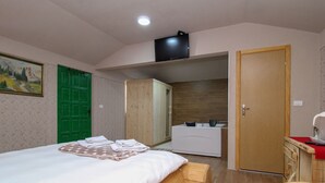 A bedroom with a bed, a green door, a wooden wardrobe, a bathroom with a sink and mirror, and a television on the wall. - Ethno Village Dolina Mira - One Bedroom Holiday Home (Drina) (Pale)