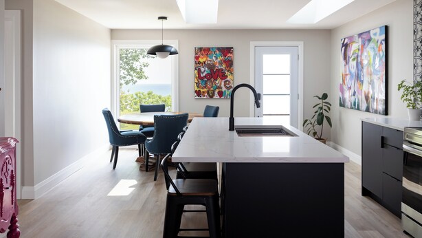 A modern kitchen with a central island, a dining area with blue chairs, and a large window with a view. - Artisan's Cove at Water's Edge by Liberty with Golf Simulator (Municipality Of Chatham-Kent)