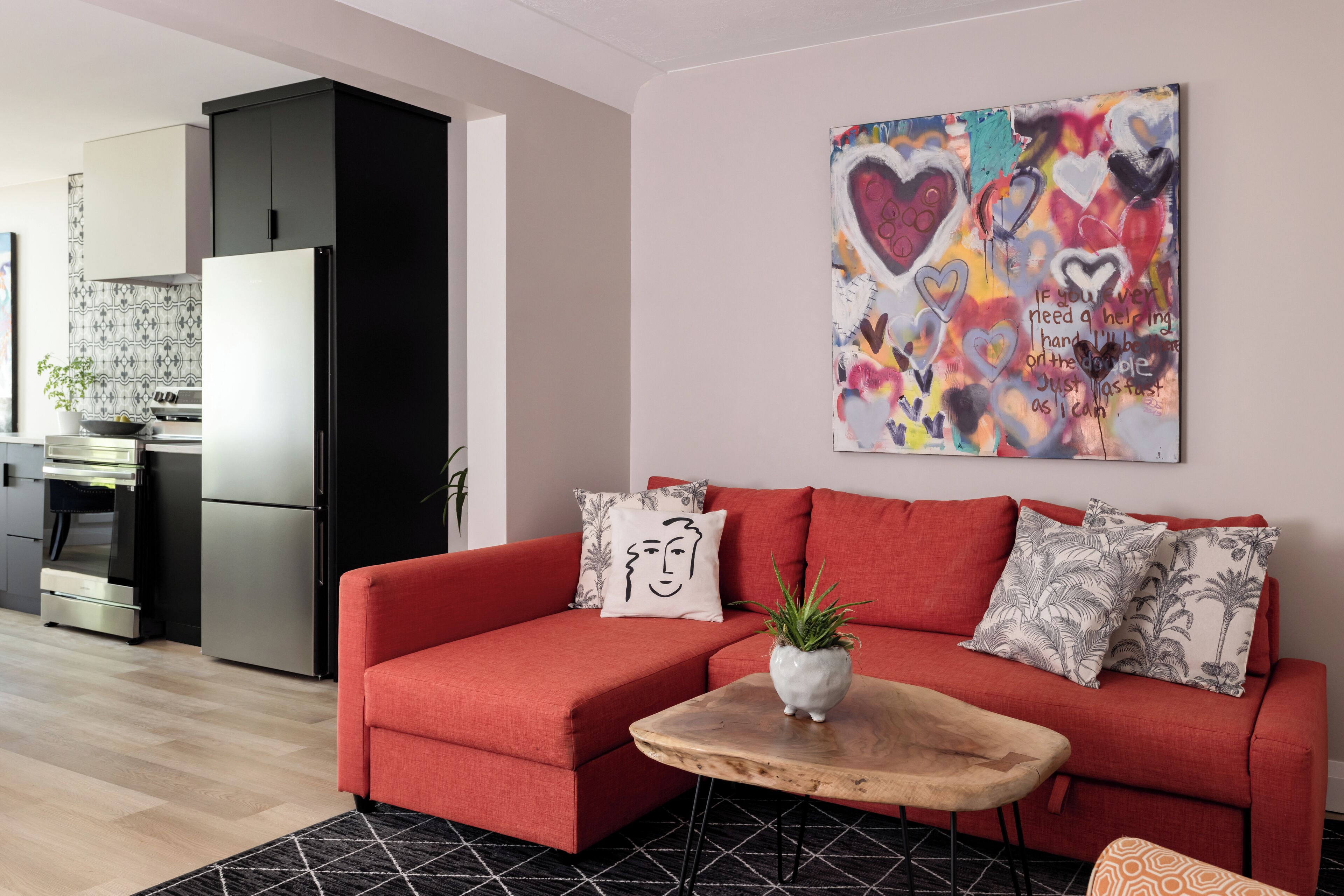Un salon moderne avec un canapé rouge, une table basse en bois et un tableau abstrait aux couleurs vives accroché au mur.