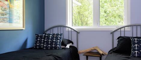Un dormitorio con dos camas individuales, una ventana que da a árboles y un ventilador de techo.