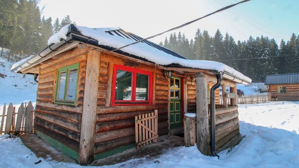 Una baita di legno con porta verde e cornici rosse, immersa nella neve.