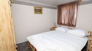 Camera da letto con una struttura letto in legno, biancheria bianca, un comodino in legno, un piccolo tavolo con una lampada e un quadro appeso al muro.