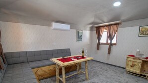 Una stanza con un divano grigio, un tavolo in legno ricoperto da una tovaglia rossa, un armadietto in legno e un condizionatore d'aria a parete.