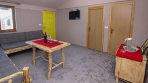Ett rum med ett träbord, en röd duk, en soffa och två trädörrar.