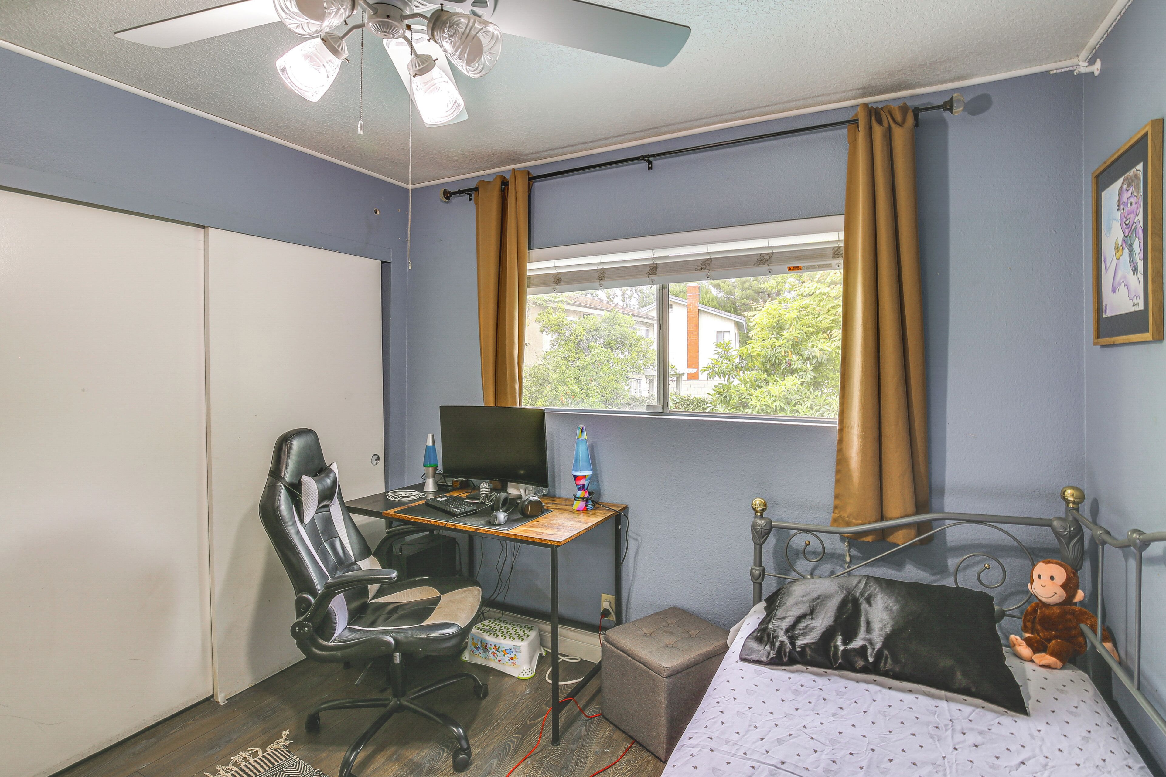 Une chambre à coucher avec un lit, un bureau avec un ordinateur, une chaise et une fenêtre avec des rideaux.