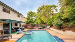 Un jardin avec une piscine, un espace salon extérieur et une terrasse couverte.