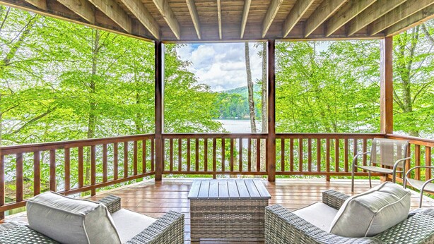 Eine überdachte Terrasse im Freien mit Korbmöbeln und Blick auf einen von Bäumen umgebenen See.