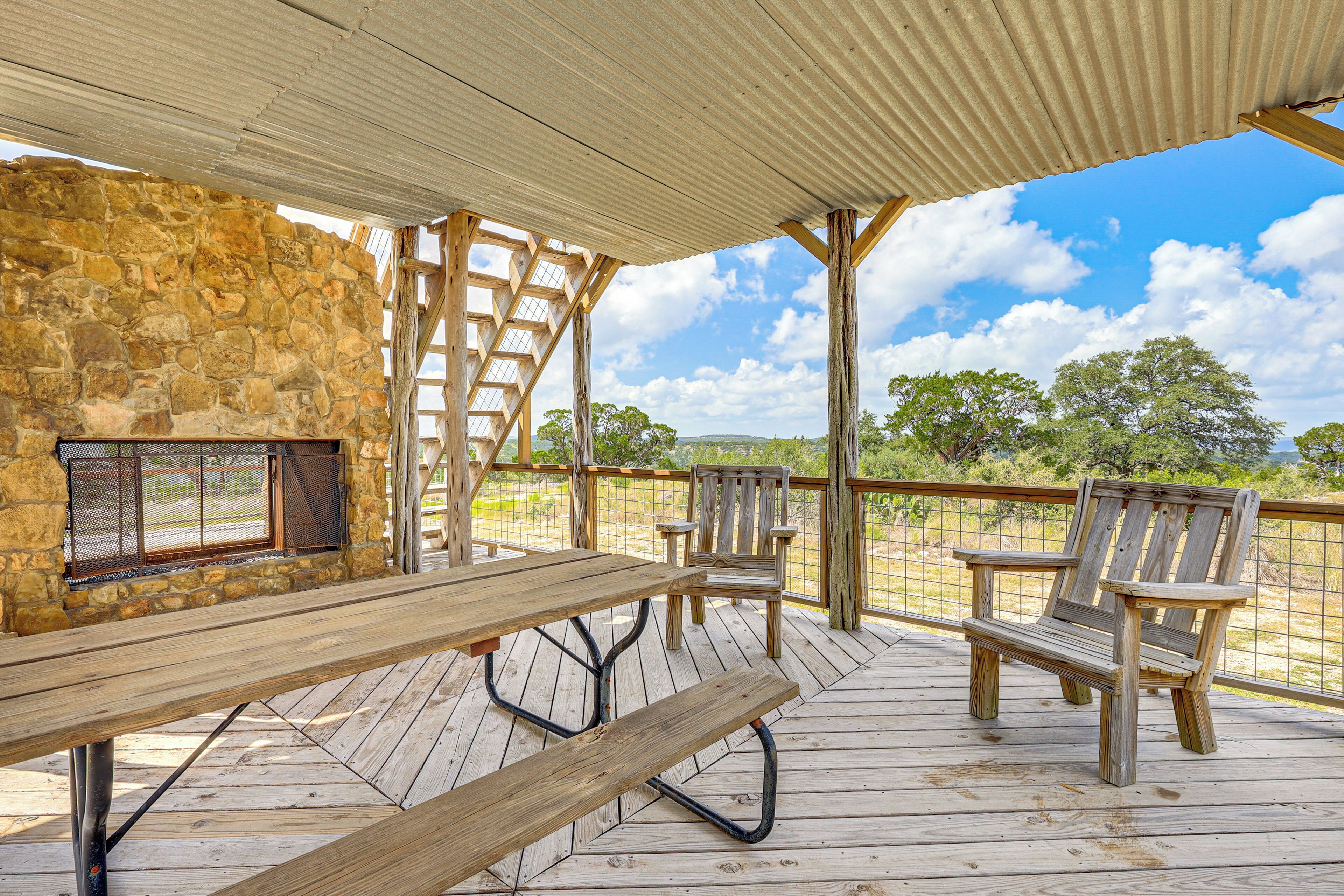 An outdoor patio with a stone wall, a wooden table, two chairs, and a metal grill.