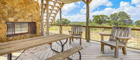 An outdoor patio with a stone wall, a wooden table, two chairs, and a metal grill.