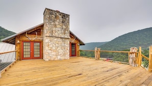 Une terrasse en bois avec une cheminée en pierre, des portes rouges et une vue sur une montagne.