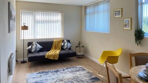 Una sala de estar con sofá, sillón amarillo y una mesa de comedor.