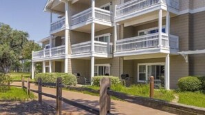 A multi-story building with balconies, a paved walkway, and a landscaped area with mulch and plants.