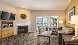 A living room with a fireplace, a television, patterned furniture, and a view through the glass doors.