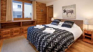 Une chambre à coucher avec une tête de lit en bois, un grand lit avec une literie à motifs, une fenêtre avec des rideaux, un tableau représentant un animal accroché au mur et une lampe de chevet.