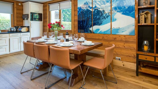 Un intérieur en bois comprenant une table à manger pour six personnes, un coin cuisine et une grande fenêtre donnant sur les montagnes.