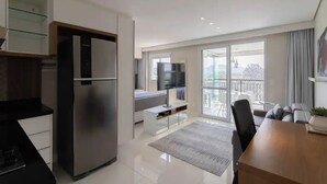 A modern kitchen with a built-in refrigerator, a dining area with a wooden table, and a balcony with a view. - Beautiful Studio - GRU 1112 (Jardim Flor da Montanha Guarulhos)