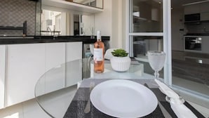 A modern dining area with a glass table, white plate, and a bottle of wine. - Beautiful Studio - GRU 1112 (Jardim Flor da Montanha Guarulhos)