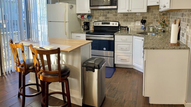 Een moderne keuken met witte kasten, een roestvrijstalen koelkast, een ingebouwde oven en een koffiezetapparaat. Er is een eethoek met houten stoelen en een tafel.