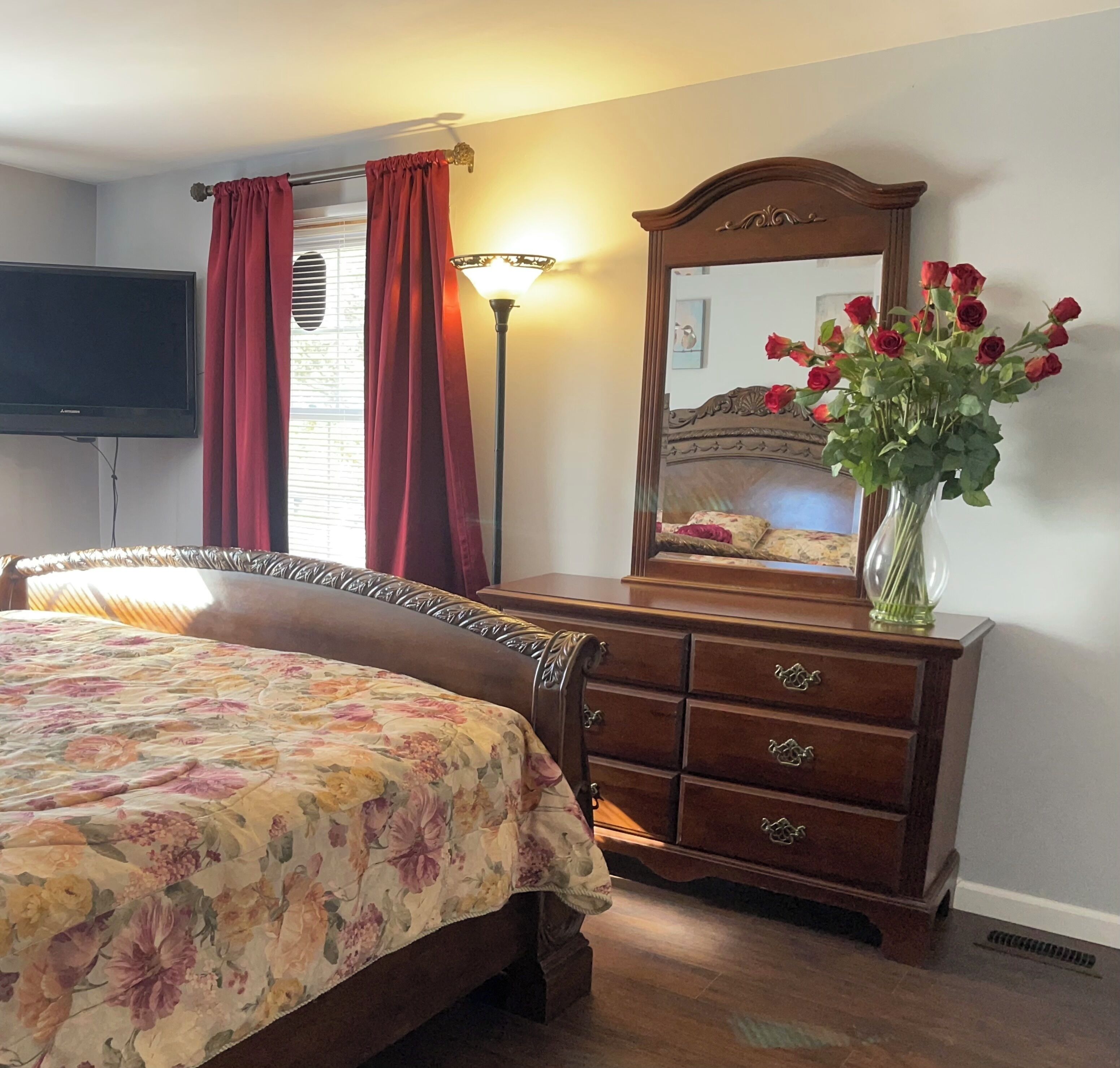 Quarto com cama, penteadeira, espelho e um vaso de flores.