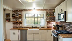 Una cocina con armarios blancos, pared de ladrillo, una ventana y un microondas integrado.