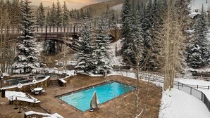 A pool area with a wooden deck, surrounded by snow-covered trees and a mountainous backdrop. - Ski In, Ski Out 1 Bedroom at the Eagle Bahn Gondola in Lionshead (Vail)
