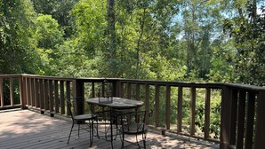 Eine Holzterrasse mit Tisch und Stühlen, umgeben von einem Geländer und dichter Vegetation.