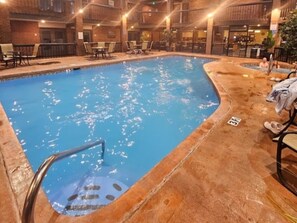 An indoor swimming pool with a clear water surface, surrounded by lounge chairs and tables.