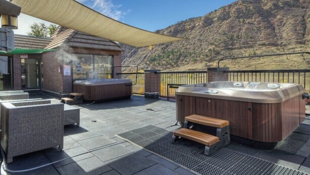 Een terras buiten met twee jacuzzi's, een overdekte zithoek en een berg op de achtergrond.
