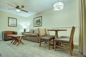 A living room with a sofa, two chairs, a coffee table, a ceiling fan, and two framed pictures on the wall.