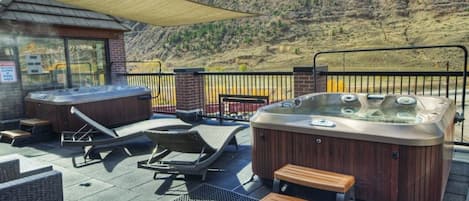 A hot tub area with lounge chairs and a wooden bench, overlooking a mountainous landscape.