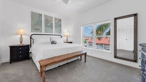 Una camera da letto con un letto, due comodini con lampade, una panca, un'ampia finestra vista edifici e una ventola a soffitto.