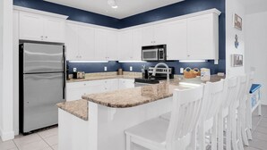 Una cucina moderna con mobili bianchi, un frigorifero in acciaio inossidabile, un forno a microonde e un piano di lavoro in granito.
