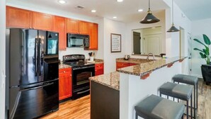 A modern kitchen with black appliances, wooden cabinets, granite countertops, and a bar area with stools.