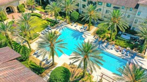 A hotel with a swimming pool surrounded by palm trees and lounge chairs.