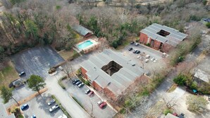 Vue aérienne d’une propriété comprenant une piscine, un parking et deux bâtiments en briques.