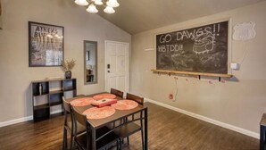 Un coin repas avec une table en bois, des chaises et un tableau noir fixé au mur, sur lequel on peut écrire.