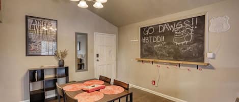 A dining area with a wooden table, chairs, and a chalkboard with writing on the wall.