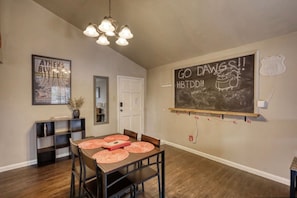 Een eetgedeelte met een houten tafel, stoelen en een prikbord met tekst op de muur.