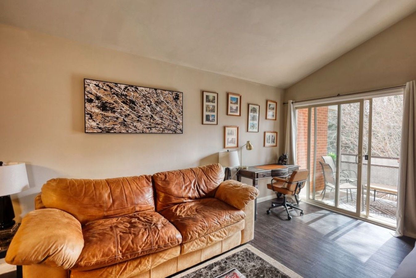 Un salon avec un canapé en cuir, un bureau avec une chaise et une grande fenêtre donnant sur les arbres.