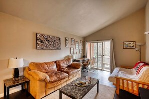 Un salon avec un canapé en cuir marron, une table basse en verre, un lit en bois et une porte-fenêtre coulissante donnant sur un balcon.