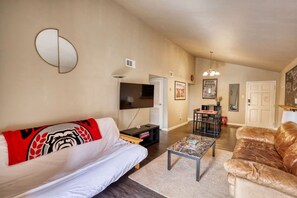 A living room with a sofa, a coffee table, a TV, and a dining area with chairs and a table. - Walk to Sanford Stadium/DT w/view Dawg Friendly! (Athens)