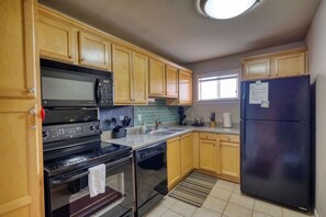 Una cocina con armarios de madera, un refrigerador negro, un microondas, una estufa y un lavavajillas.
