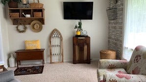 Una sala de estar acogedora con televisión, estanterías de madera, un adorno en la pared, una cesta de mimbre y un sofá estampado con motivos florales.